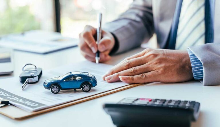A person holding auto loan documents and car keys next to a parked modern car.
